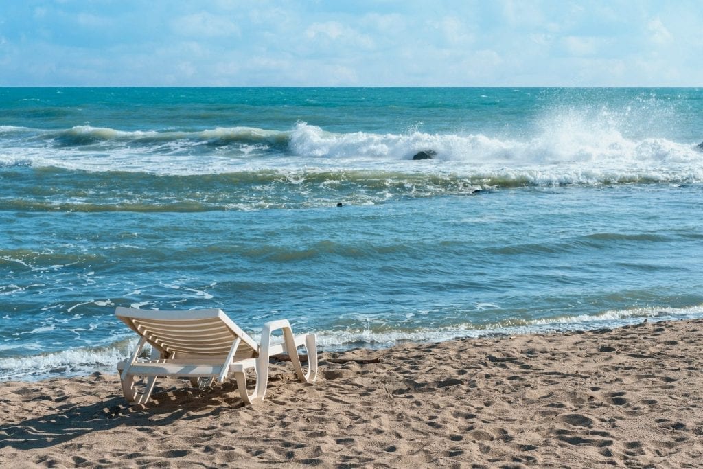在Ostia Lido海滩边的白色躺椅上，大海和一个海浪占据了照片的大部分