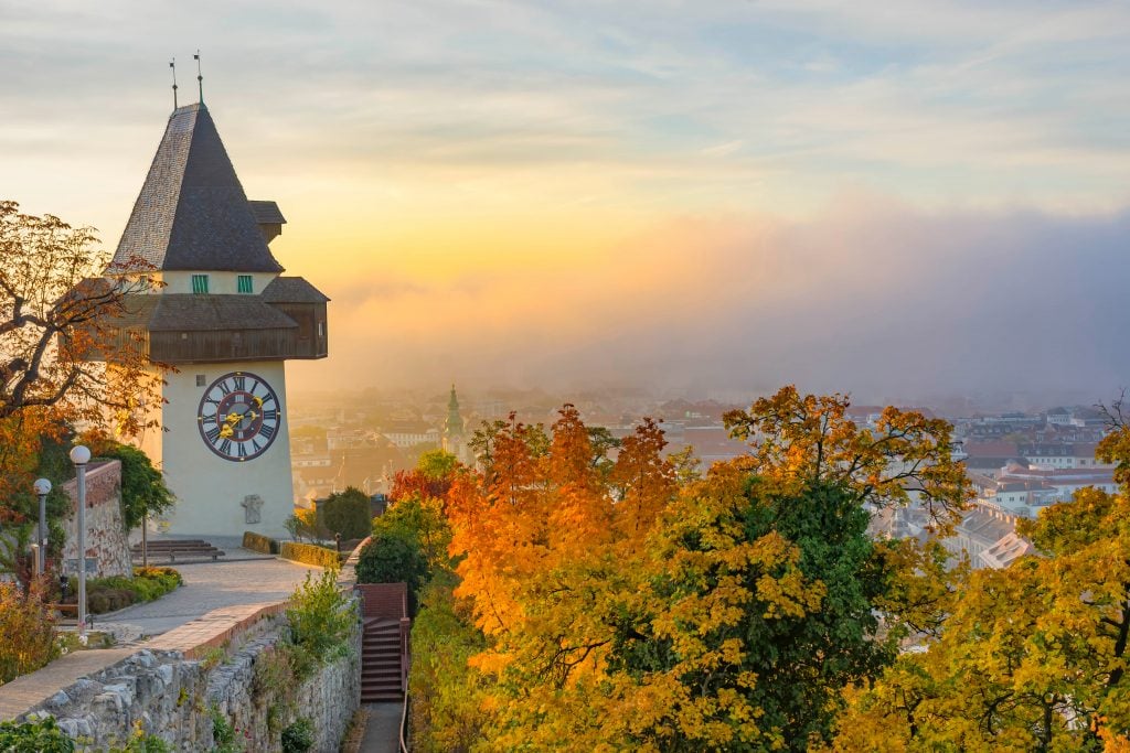 日落时分的格拉茨奥地利钟塔，前景是秋天的树叶