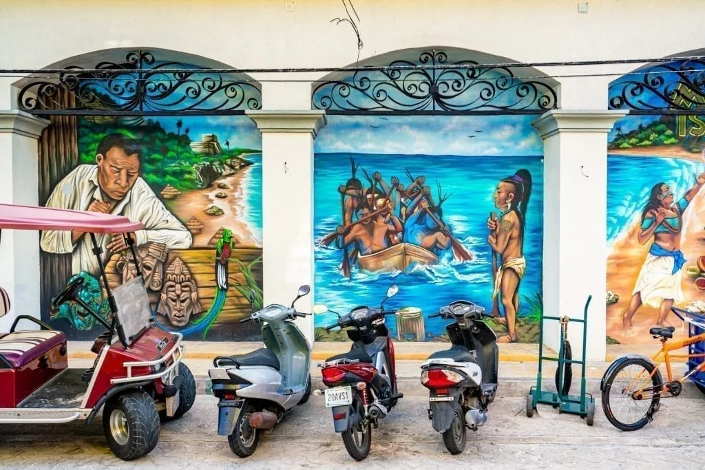 墨西哥Isla Mujeres的街头艺术，轻便摩托车和一辆高尔夫球车停在它所在的建筑物前。街头艺术描绘了玛雅文化。