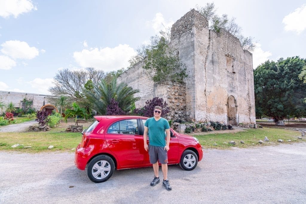 杰里米·斯道姆站在一辆停在教堂前的红色汽车前，这是他尤卡坦半岛自驾游行程的一部分