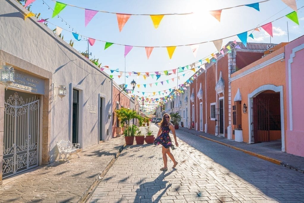 凯特·斯道姆在尤卡坦半岛自驾游时，站在墨西哥瓦拉多利德一条五颜六色的街道上，街道上悬挂着旗帜