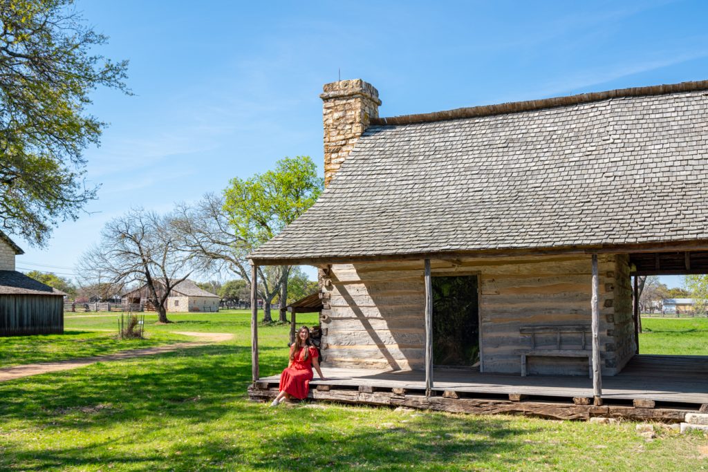 凯特身穿红色连衣裙出现在约翰逊市的一座历史建筑前，这里是德克萨斯州最好的周末度假胜地之一