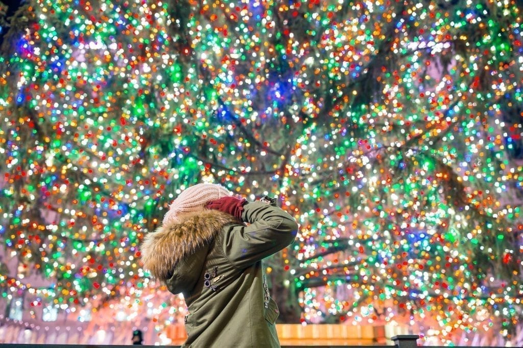 一名身穿绿色外套的女子抬头望着挂满彩灯的洛克菲勒圣诞树。纽约是美国经典的圣诞度假胜地