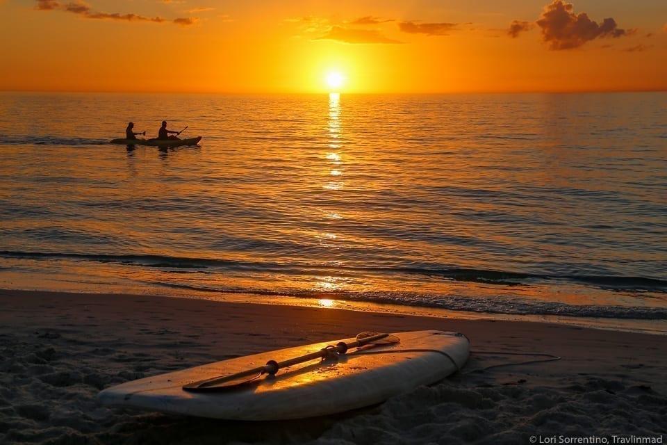 佛罗里达州那不勒斯日落时的海滩，前景是一块冲浪板，水面上是明亮的橙色日落