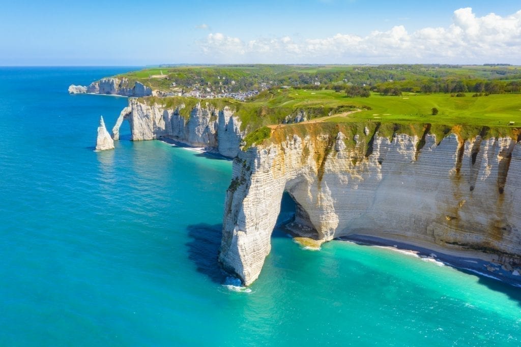 White cliffs of Etretat with bright blue water to the left side of the photo. Etretat is one of the best places to visit in France