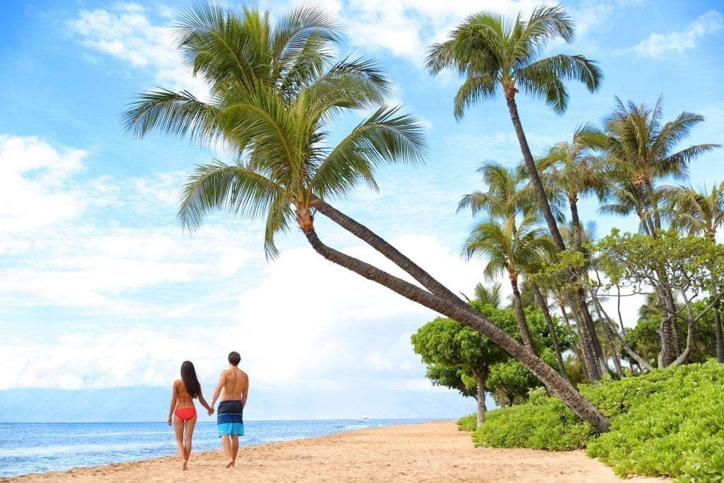 在毛伊岛的卡纳帕里海滩散步的情侣，在棕榈树的树荫下。卡那帕里海滩是美国最好的海滩之一