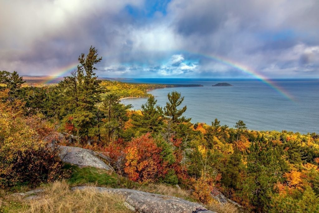 View of Lake Superior with a rainbow over it during fall foliage season on Sugarloaf Mountain in Michigan