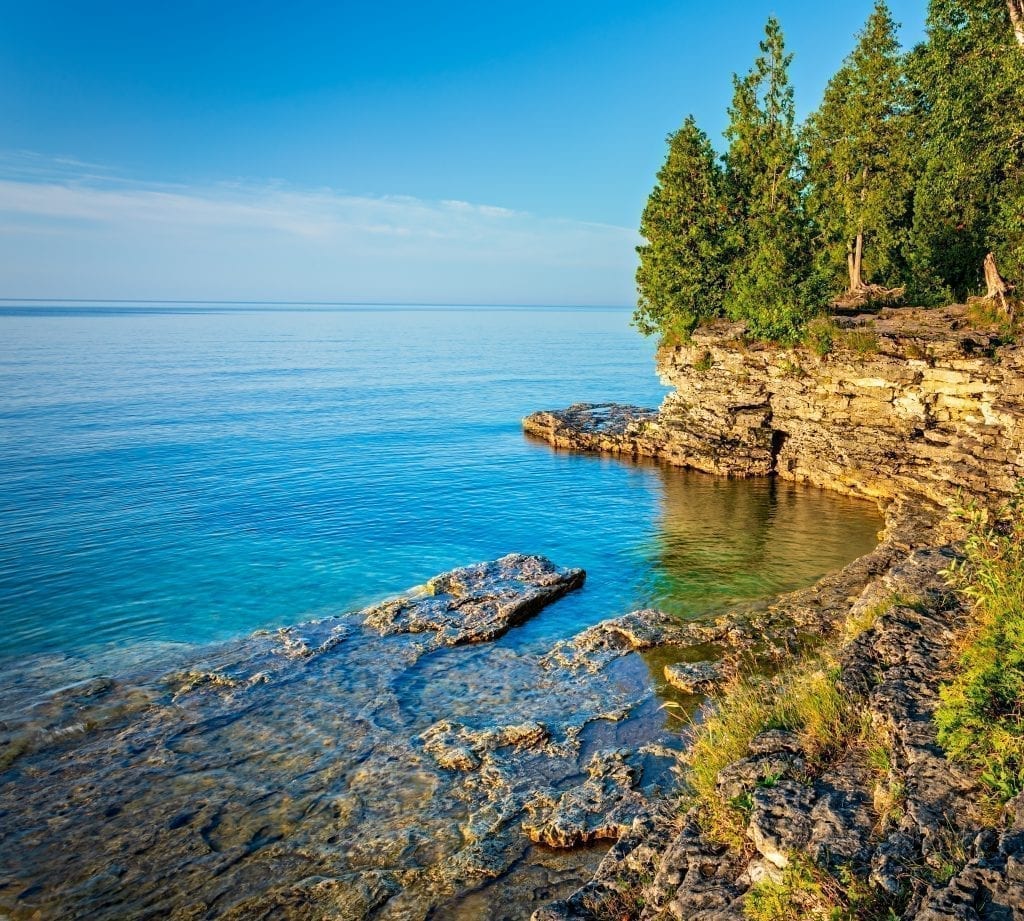 Lakeshore at golden hour in Door County Wisconsin with evergreen trees on the right side of the photo