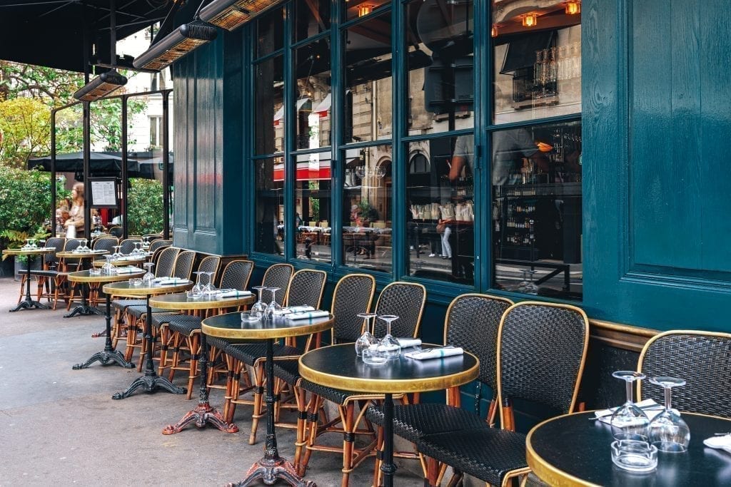 法国的咖啡馆，黑色的椅子排列在蓝绿色的建筑旁边。在法国的咖啡馆里吃一顿典型的早餐是一种很棒的体验!