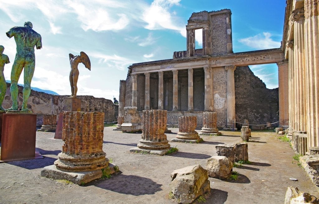 意大利庞贝的一个广场的照片，里面有柱子的废墟和几个雕像