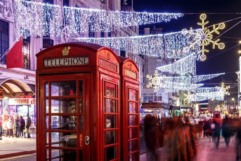 伦敦经典的红色电话亭，上面挂着圣诞彩灯，顾客从电话亭旁走过
