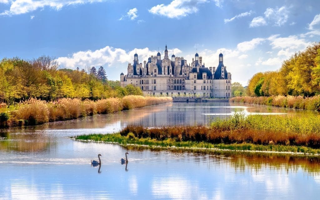 Château从远处看，前景有一个池塘，池塘上有两只天鹅