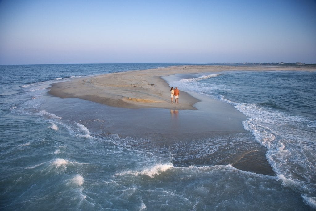 情侣站在秃头岛的沙滩上，这是北卡罗来纳州最浪漫的度假胜地之一