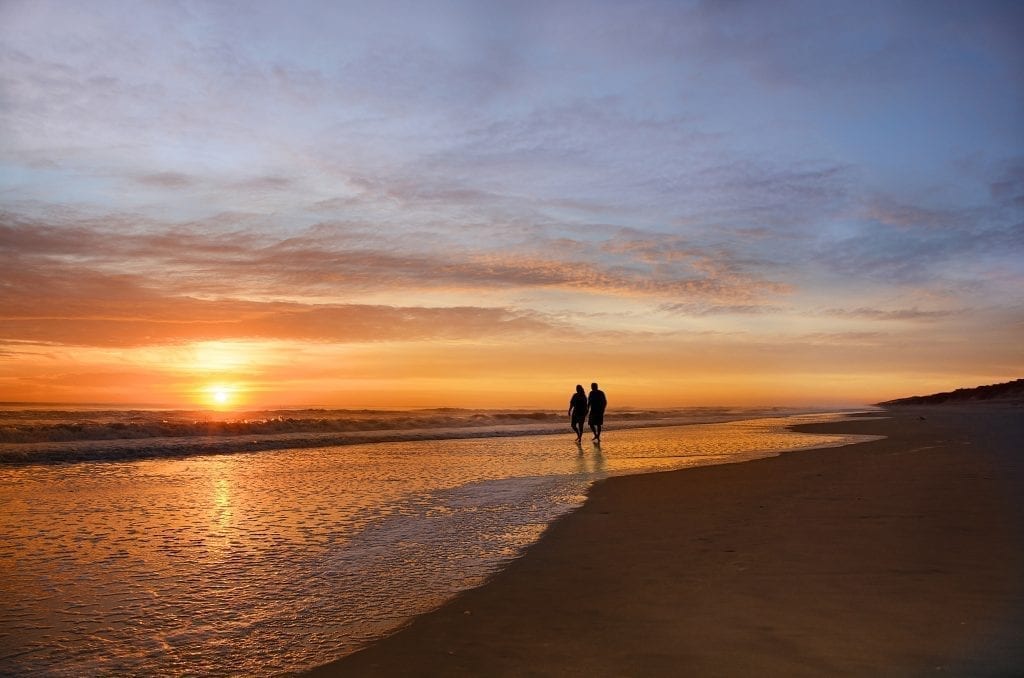 一对情侣在日落时分沿着外滩的海滩散步，这是北卡罗来纳州情侣们最浪漫的度假胜地之一