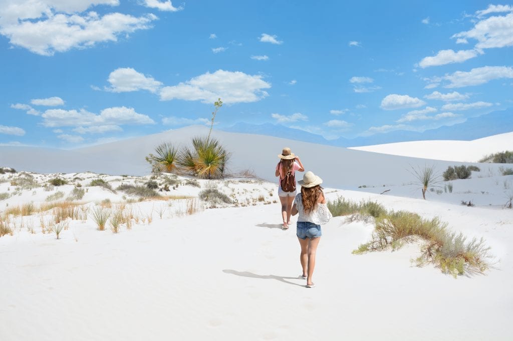 两个年轻女子在白沙国家公园的沙丘上徒步旅行，白沙国家公园是美国最美丽的国家公园之一