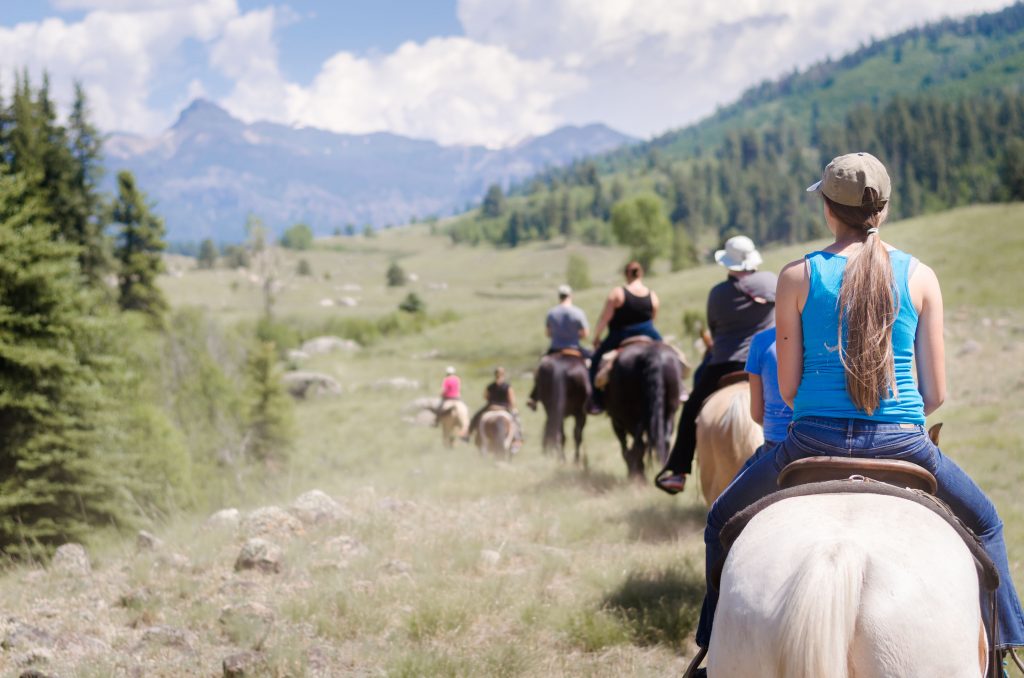 科罗拉多山上的一群骑马的人，前景中的女人骑着一匹白马