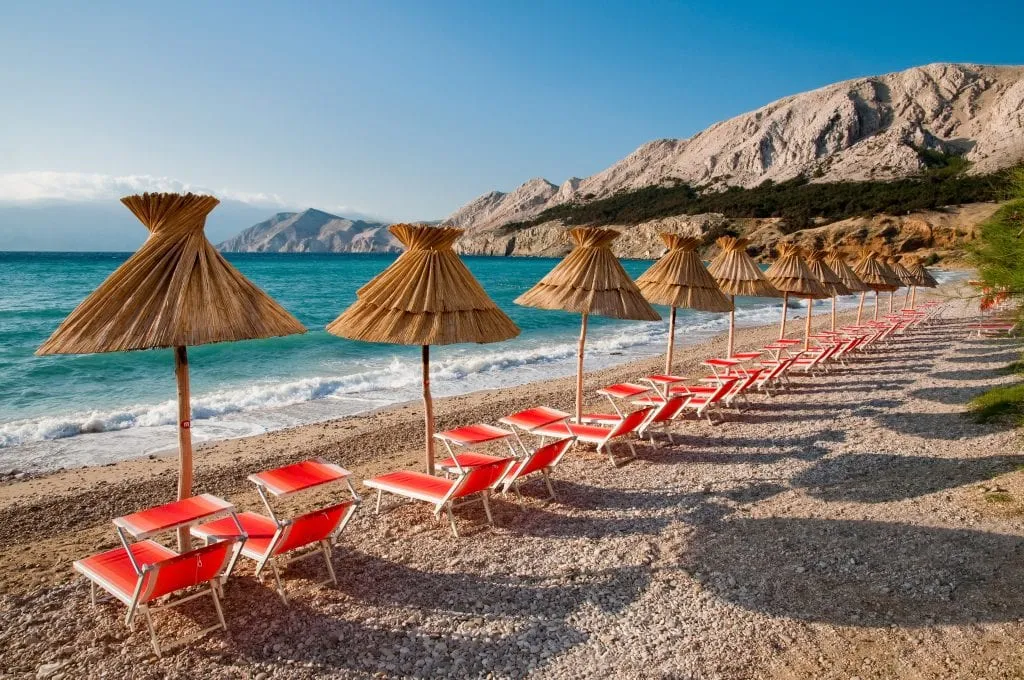 KRK岛上的小海滩，有稻草遮阳伞和红色沙滩椅