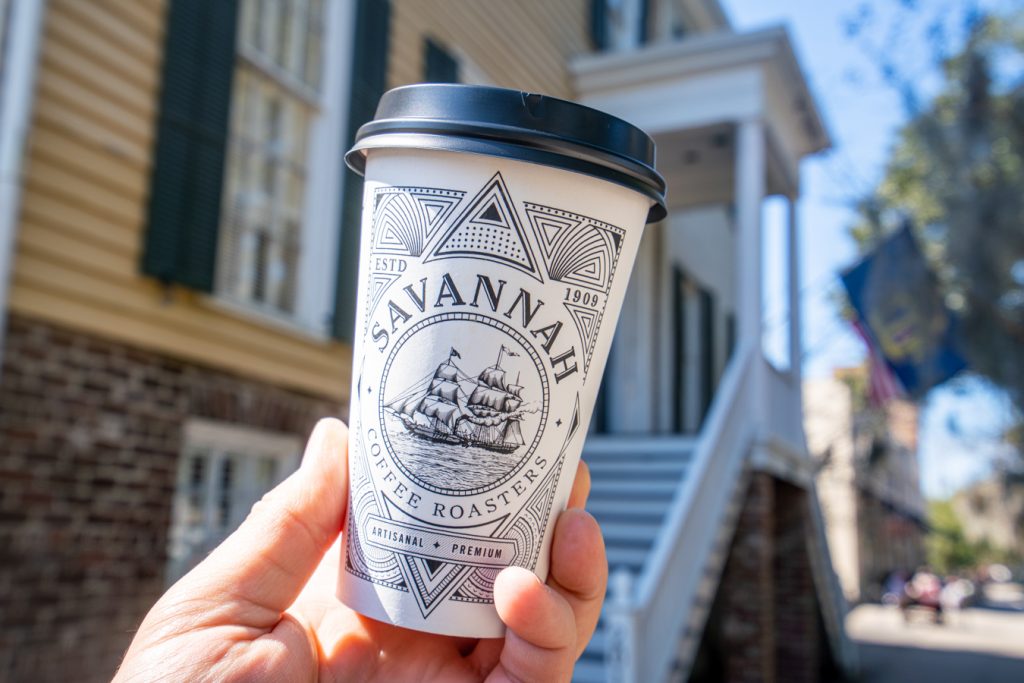 来自萨凡纳咖啡烘焙师的杯子，萨凡纳最好的咖啡店之一，被举在黄色建筑前