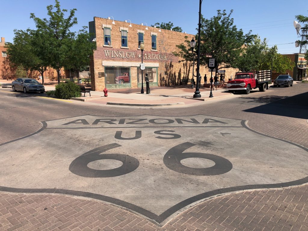 站在亚利桑那州温斯洛的角落公园的照片，前景画在地上的66号公路标志