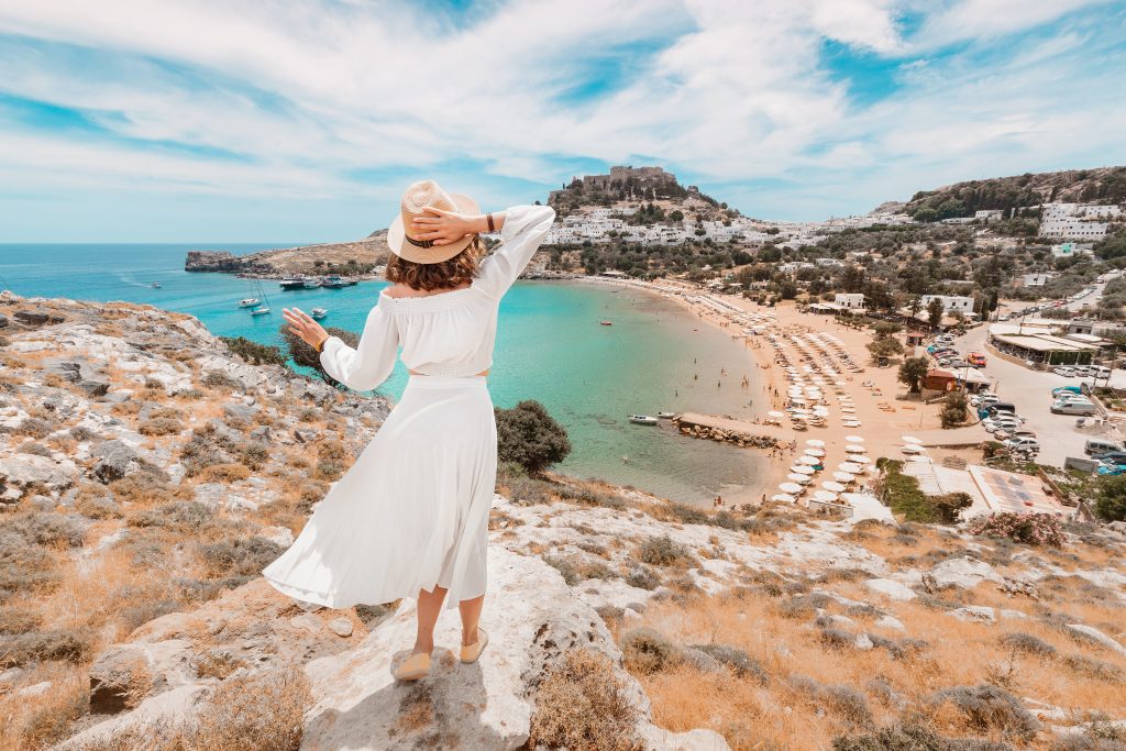 身穿白色连衣裙的年轻女子俯瞰着罗德岛的海滩，这是7天跳岛探索希腊时有趣的一站