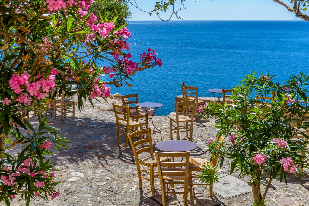 小桌子俯瞰大海，周围是粉红色的花朵，就像在希腊旅行时看到的那样