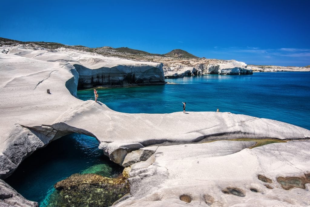 人们走过Serakiniko海滩的岩层，这是希腊7天行程中最好的景点之一