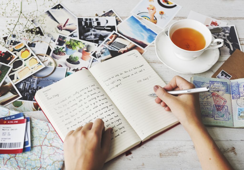 一个人在最好的旅行日记之一上写着照片，旁边放着一杯茶必威体育官方登录
