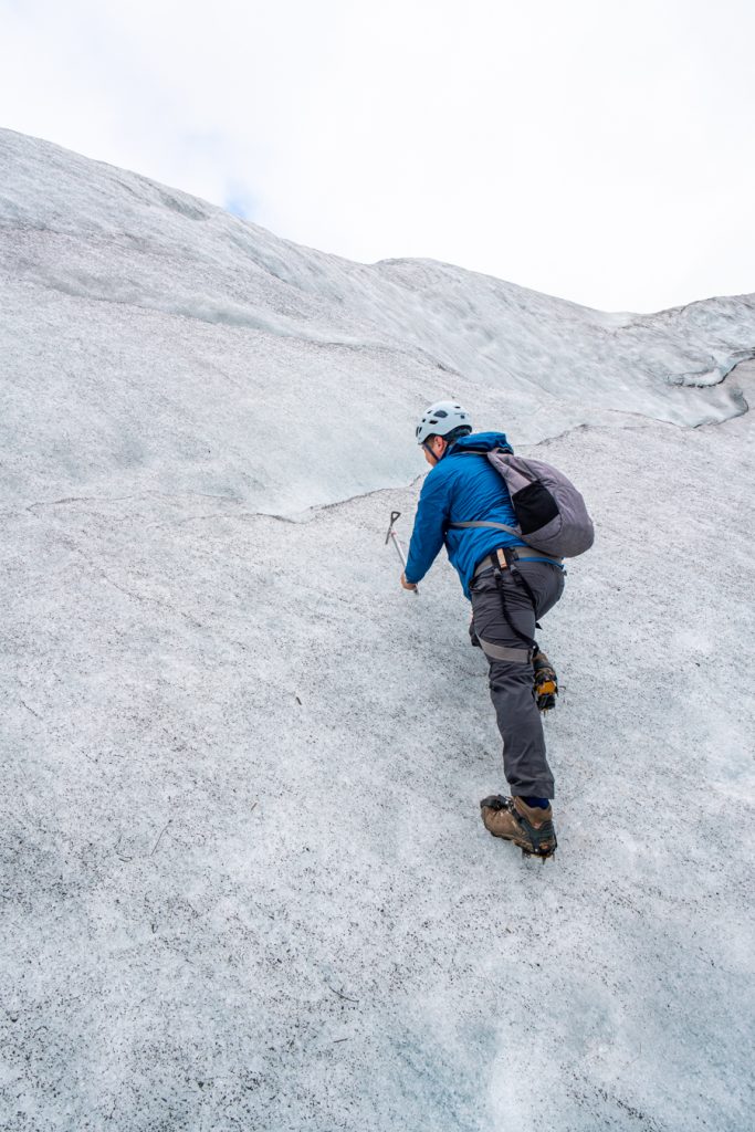 穿着蓝色夹克的杰里米·斯托姆在冰岛的冰川上摆姿势，就像在攀岩一样