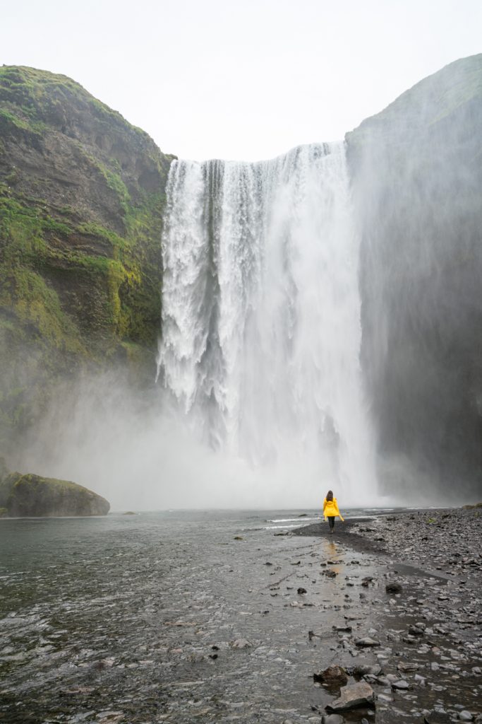凯特穿着一件黄色夹克站在skogafs前面，这是在冰岛最好的事情之一