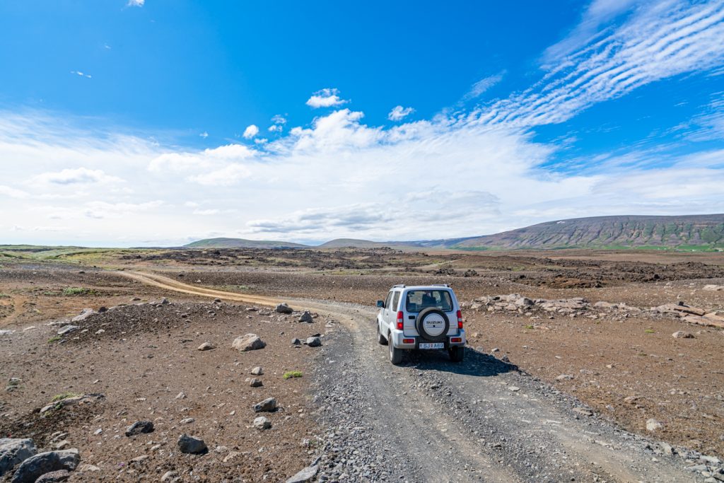 蓝色的天空下，一辆灰色的吉普车停在冰岛空旷的土路上