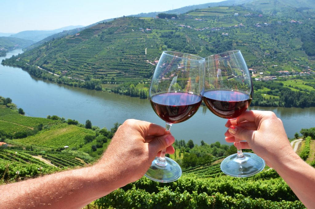 在葡萄牙的杜罗山谷前，两杯葡萄酒被举起来