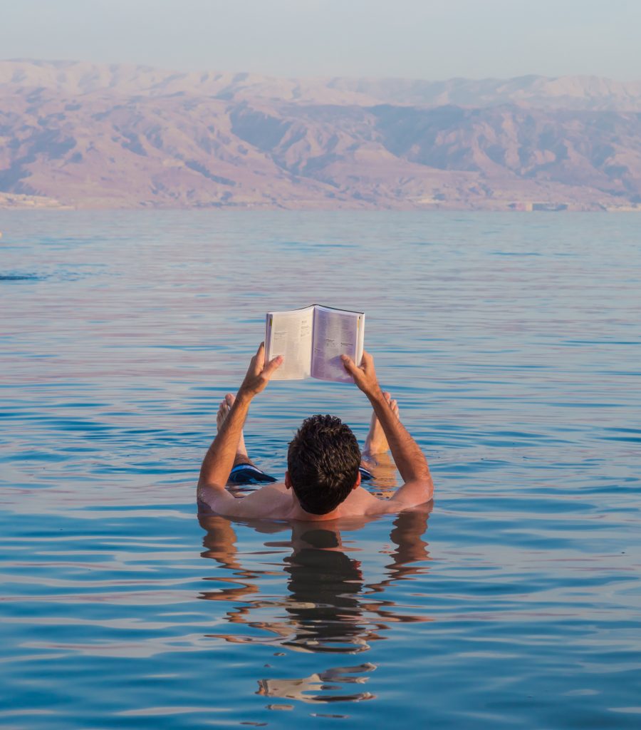 一名男子在约旦死海漂浮，手里举着一本书