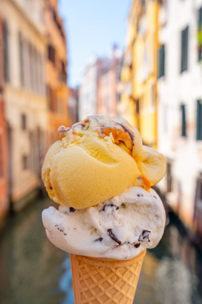在威尼斯运河前，用两个蛋筒装着冰淇淋——不吃冰淇淋绝对是在意大利不可做的事情之一