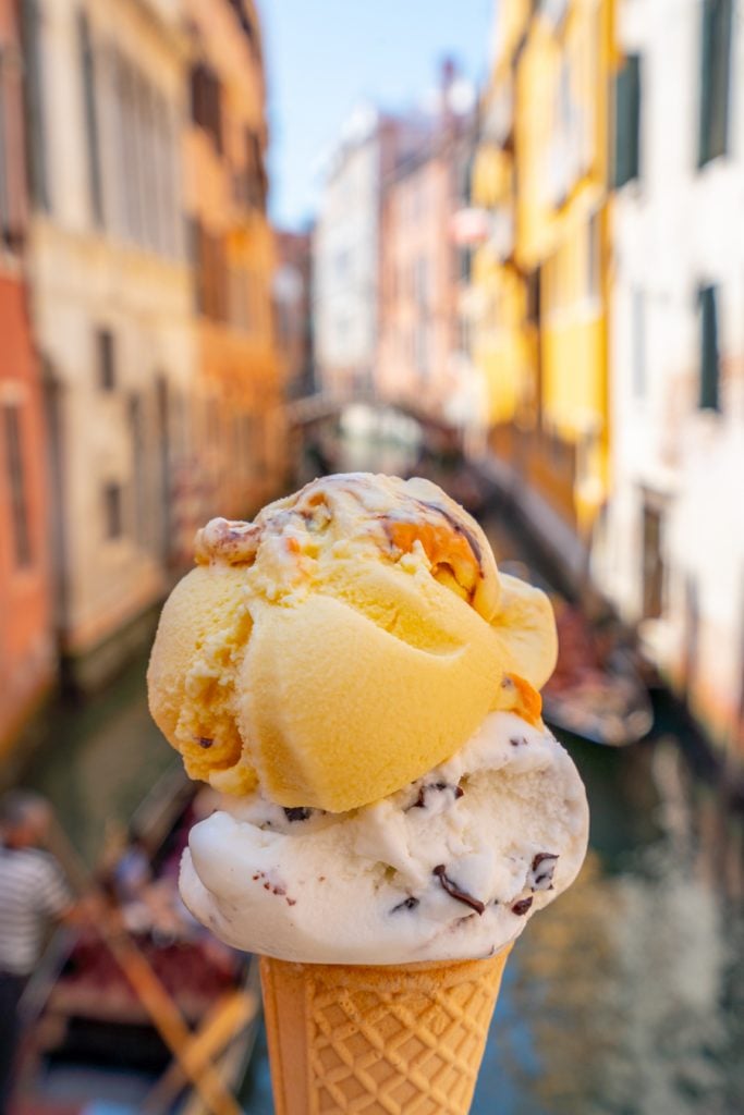 在威尼斯的夏天，人们在运河前拿着两勺冰淇淋