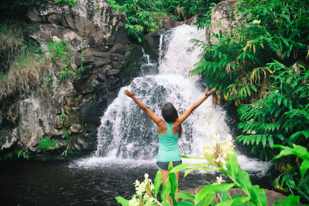 一名身穿绿色背心的女子站在waimea瀑布前，这是夏威夷瓦胡岛的最佳景点之一
