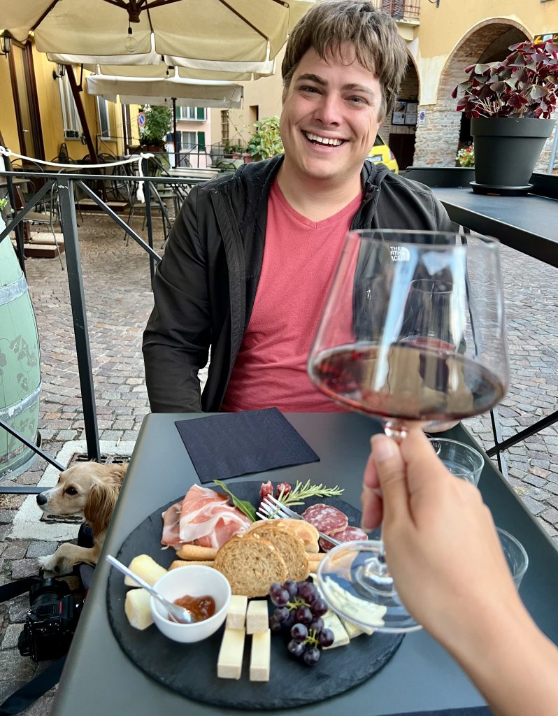 杰里米在意大利巴罗洛的一家酒吧里，面前的桌子上放着一个奶酪盘，前景上放着一个酒杯