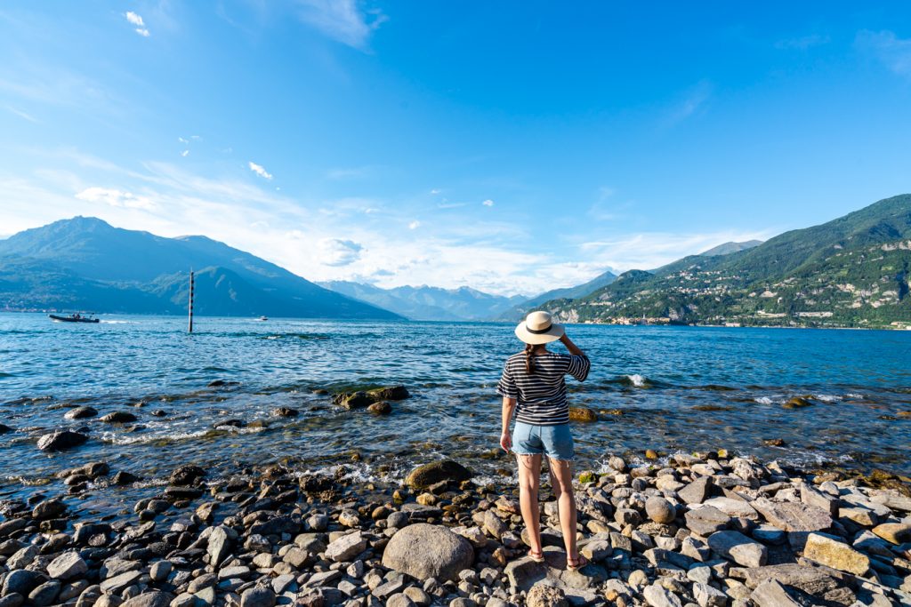 凯特穿着短裤，戴着太阳帽，从岩石海滩俯瞰科莫湖