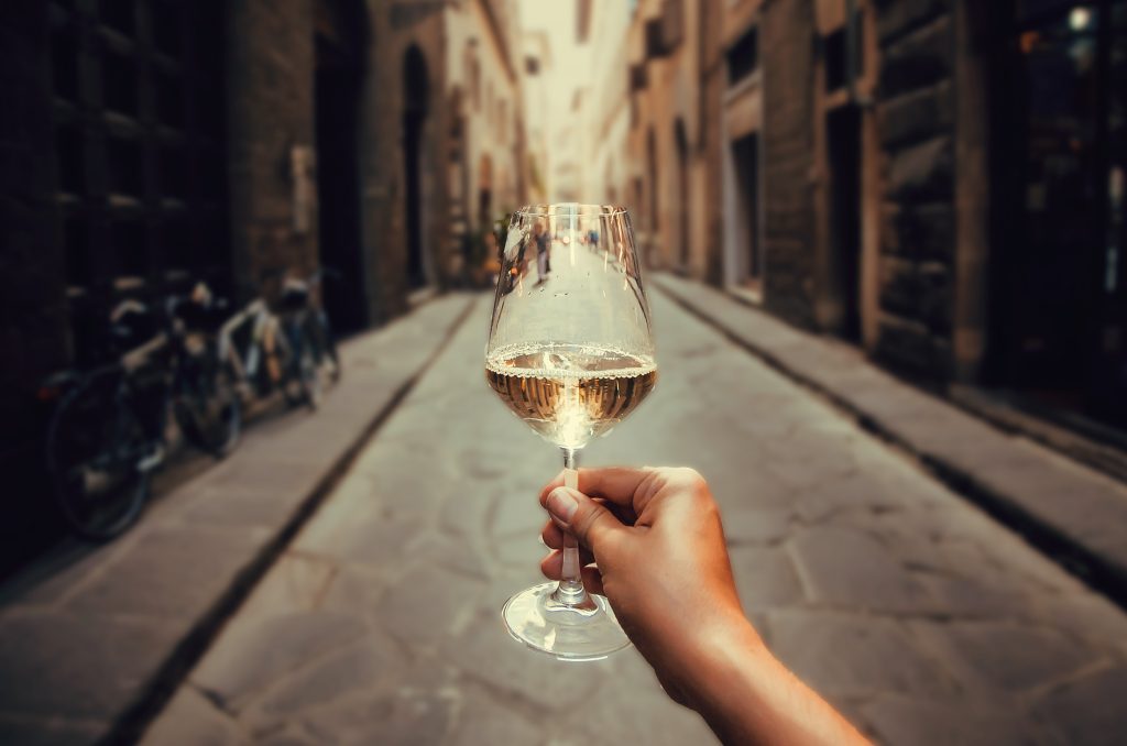 在罗马的一条铺满鹅卵石的街道上，一个人拿着一杯白葡萄酒