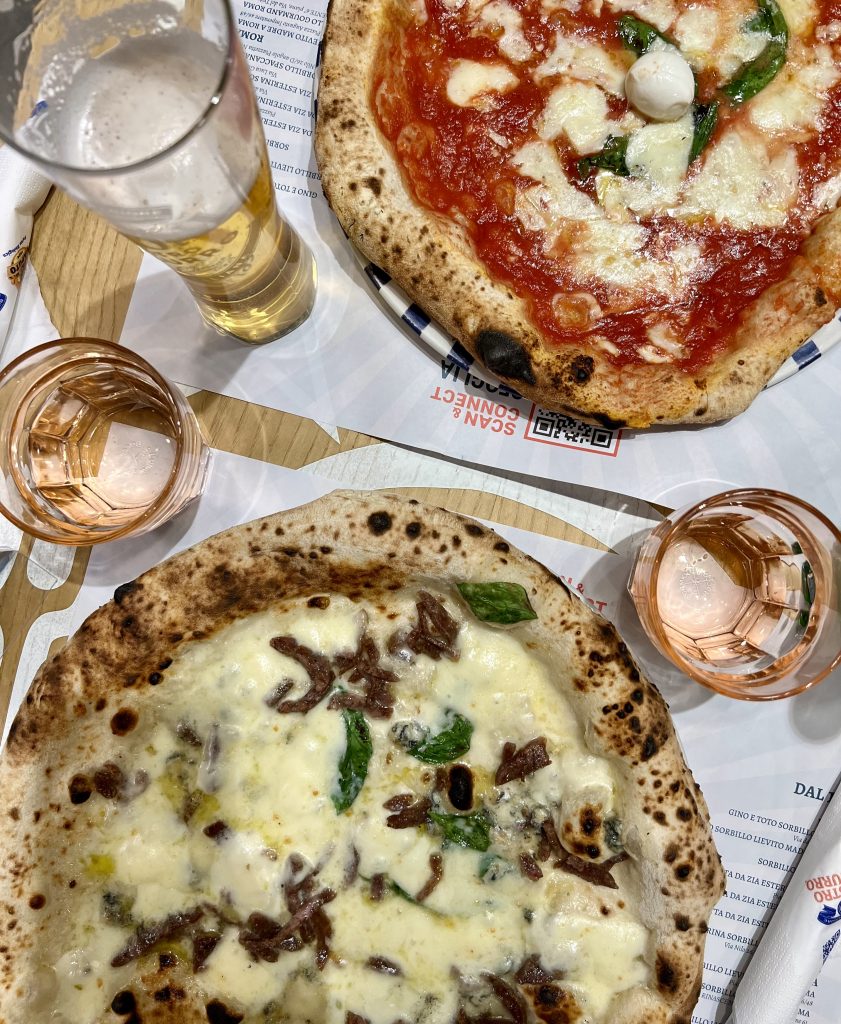 两个那不勒斯风格的披萨，桌子上放着啤酒，教你如何在意大利吃披萨