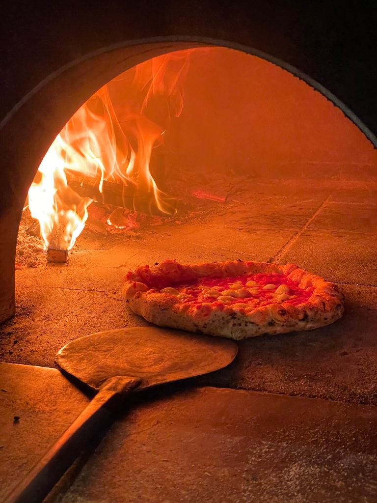 意大利披萨的近照，在燃烧木头的披萨烤箱里，披萨旁边放着桨